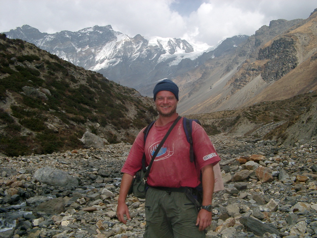 Alan on the Annapurna Circuit trek in Nepal, standing in a rocky valley beneath snow-covered peaks
